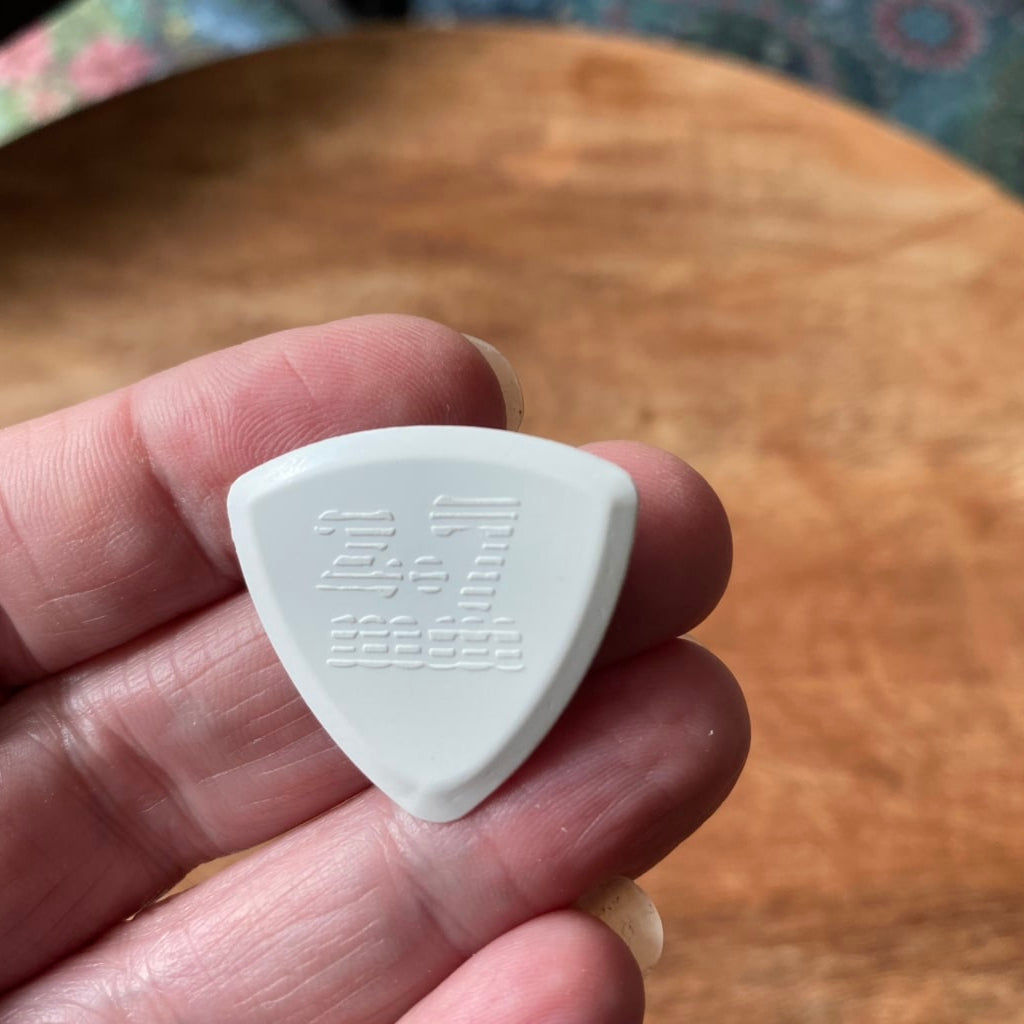 White guitar pick held in a hand with a wooden surface in the background