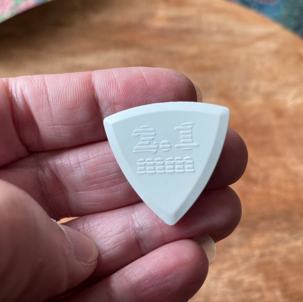 White triangular guitar pick held in a hand with a wooden surface in the background