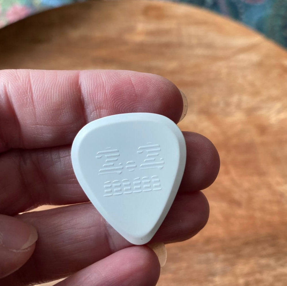 White guitar pick held in a hand with a wooden surface in the background